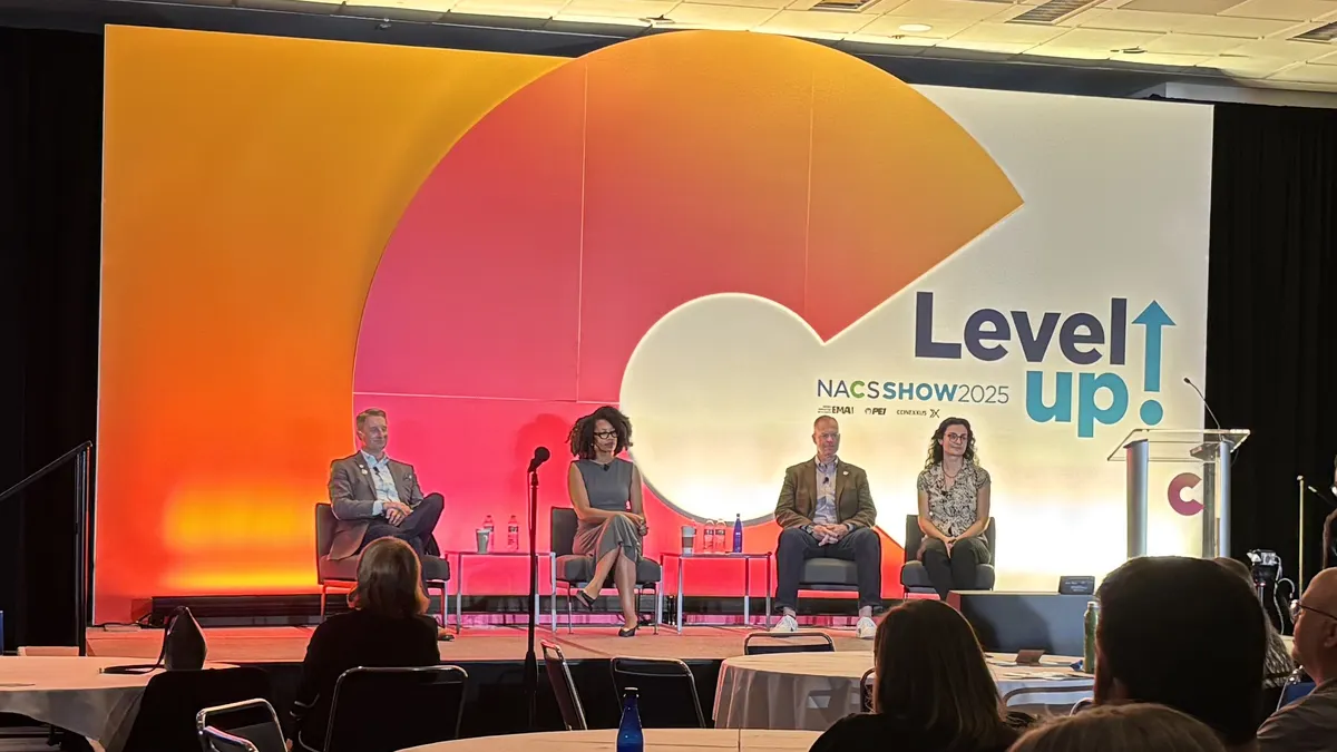 Four people sit on a stage. A sign behind them says "Level up"