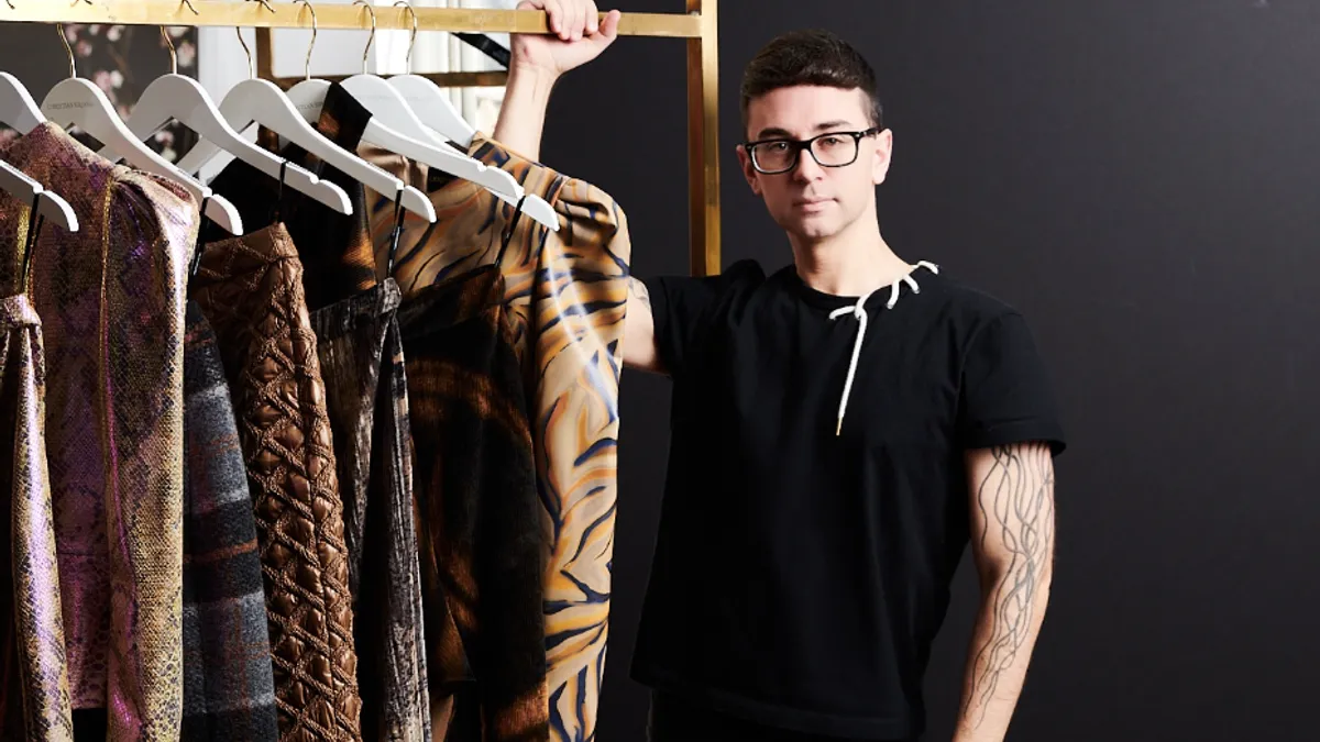 Christian Siriano stands holding a rolling rack of clothes.