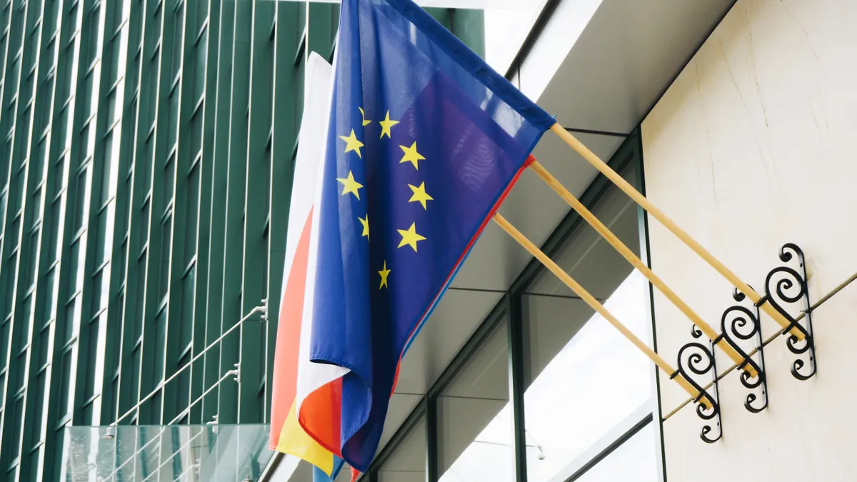 The European Union flag hags at the entrance of a modern glass office building.