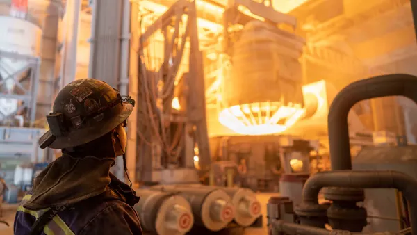 A worker wearing protective gear watching an electric furnance in the background.