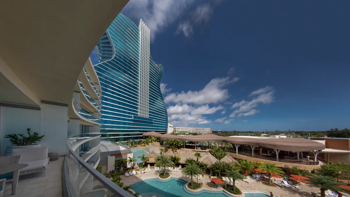 A tall, guitar shaped, window-covered building looms in the background on a very sunny day.