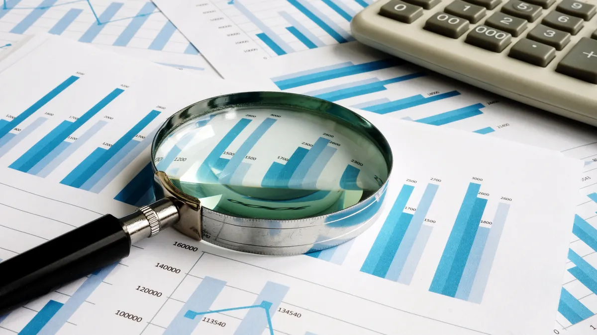 Papers with bar graphs all over a flat surface with a calculator and magnifying glass on top of them.