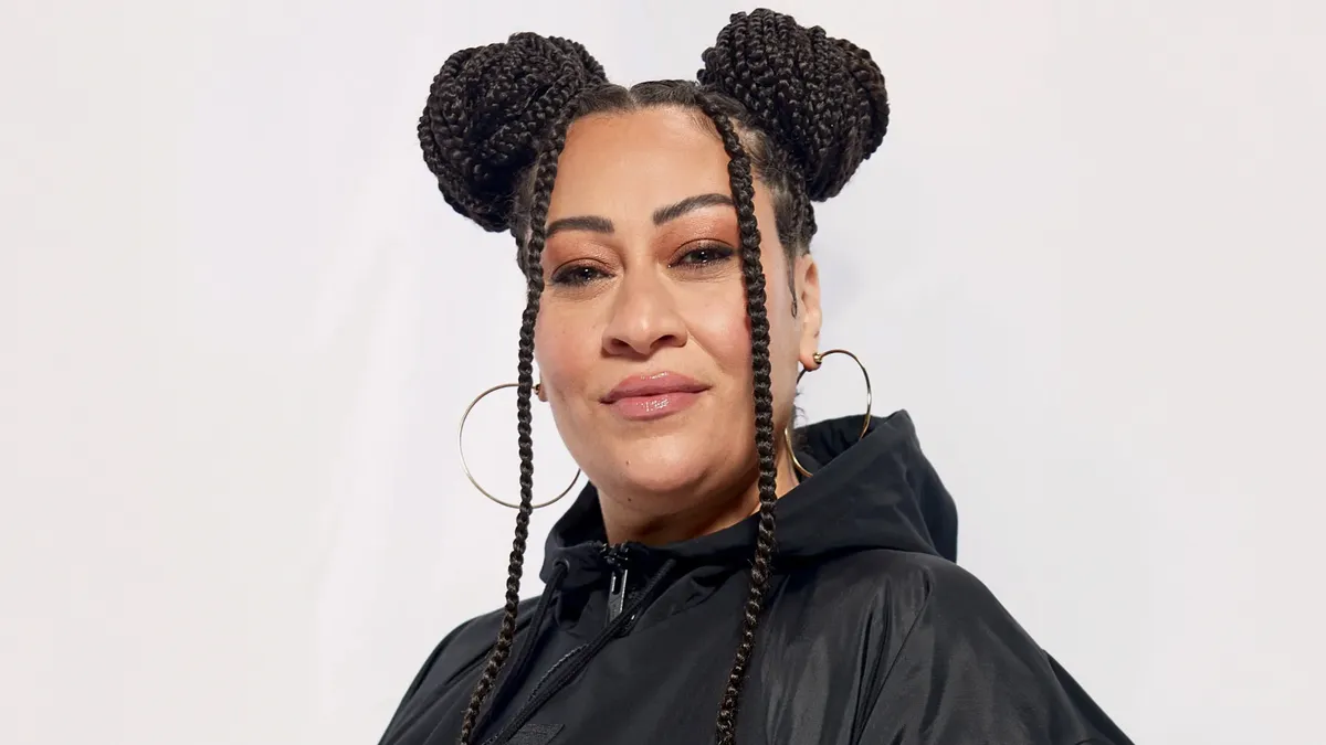 A person with braids and large hoop earrings wears a black hoodie.