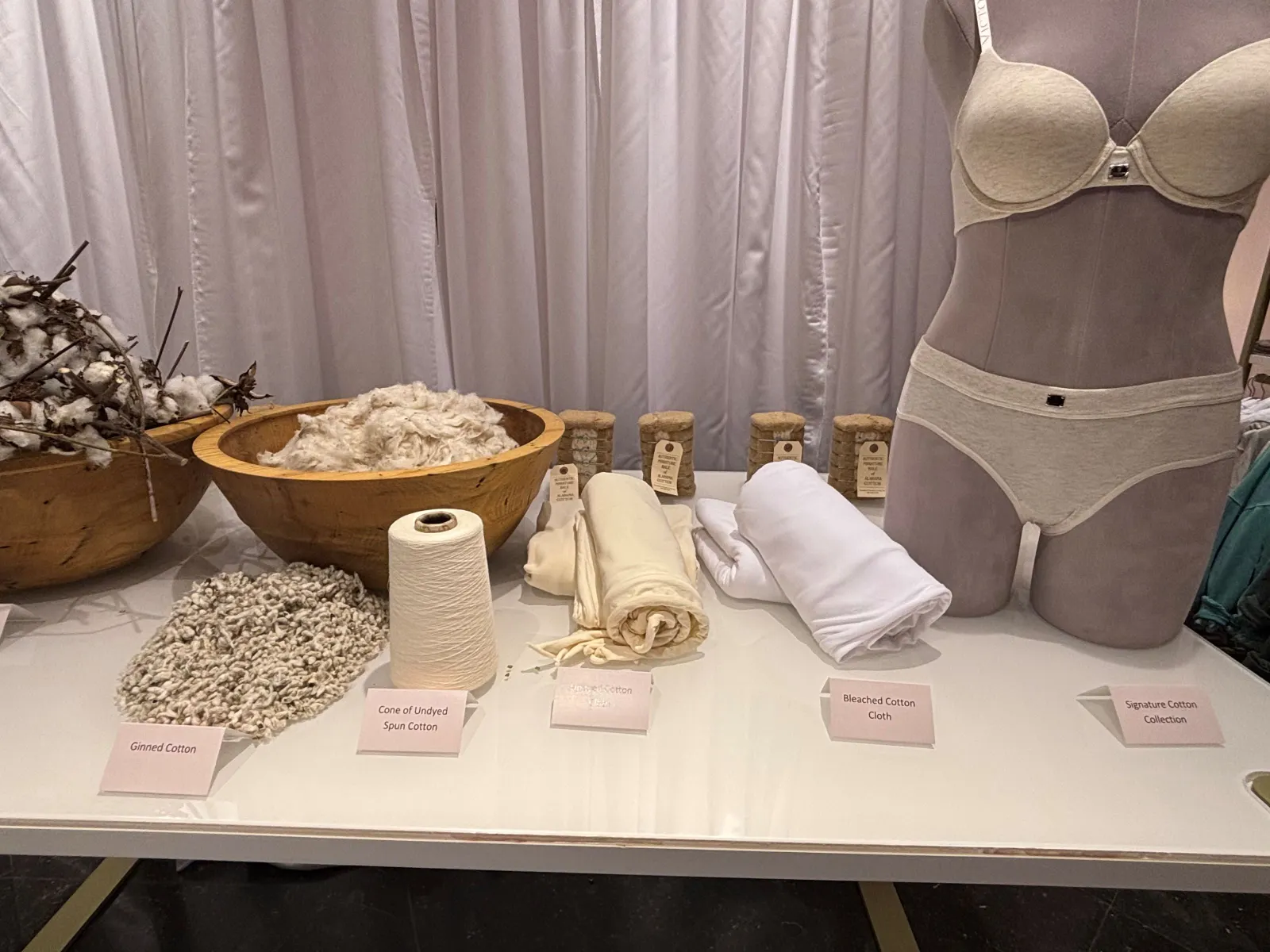 White and tan cotton material and a mannequin in a white bra and underwear on a display table