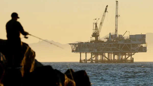 a man fishes with an offshore oil drilling rig in the background