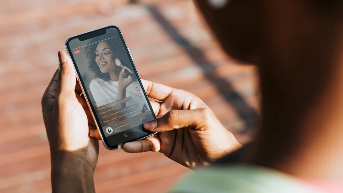 A person holds a mobile phone. On the screen is a person putting on blush.