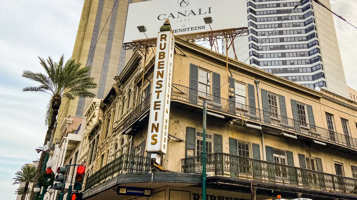 A yellow-brick corner building, with a vertical sign reading "Rubensteins," a palm tree on the left.