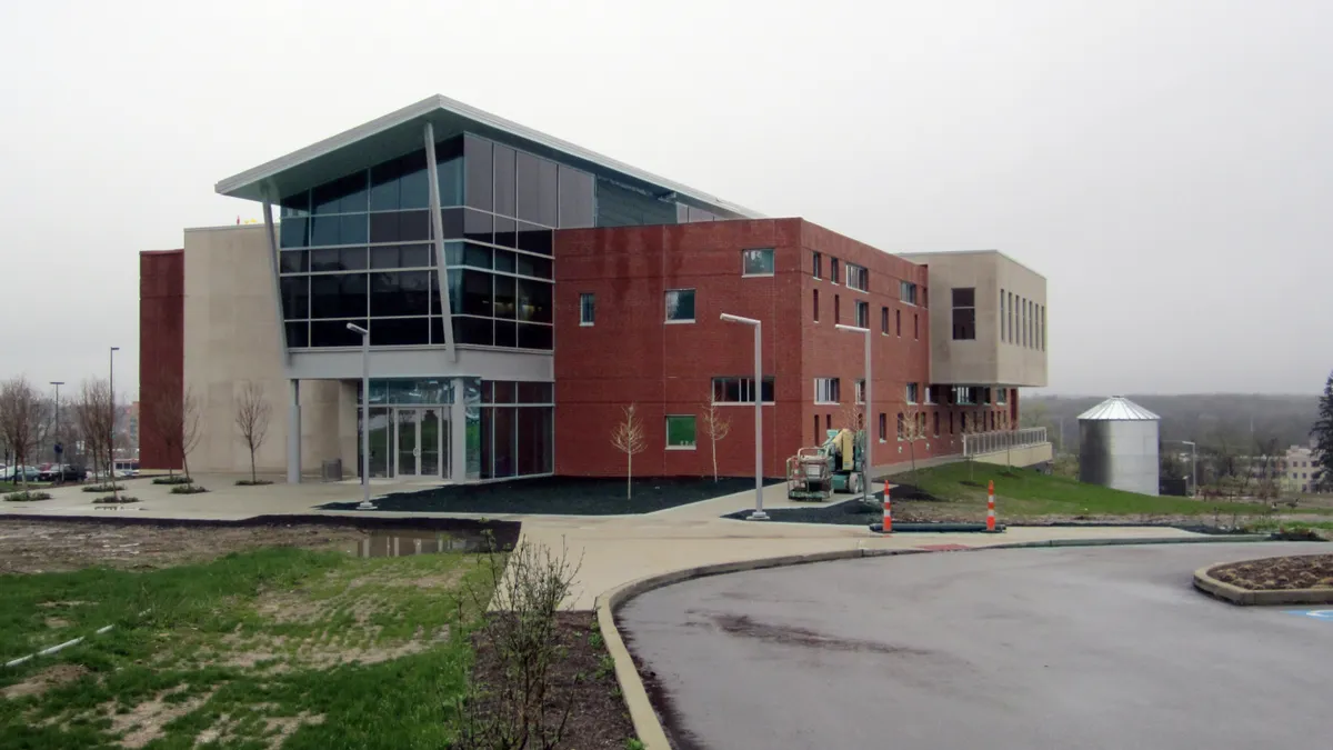 A mid-century modern academic building sits in the mid ground of the photo, in front of a grey sky on a rainy day.