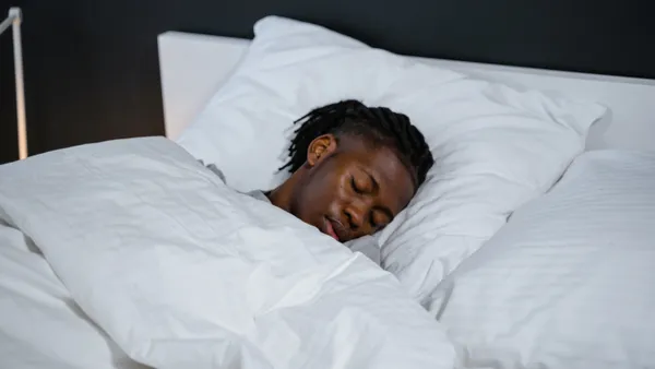 A Black man with dreads rests in-bed