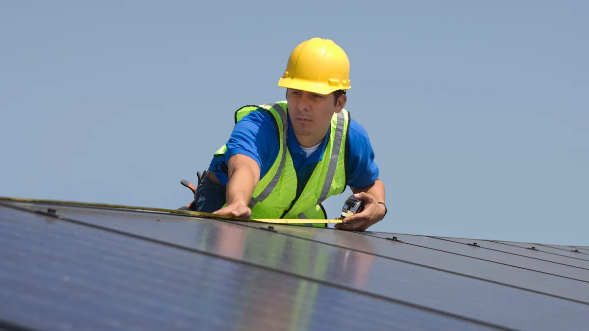 A man with a yellow helmet installs solar panels on a roof.