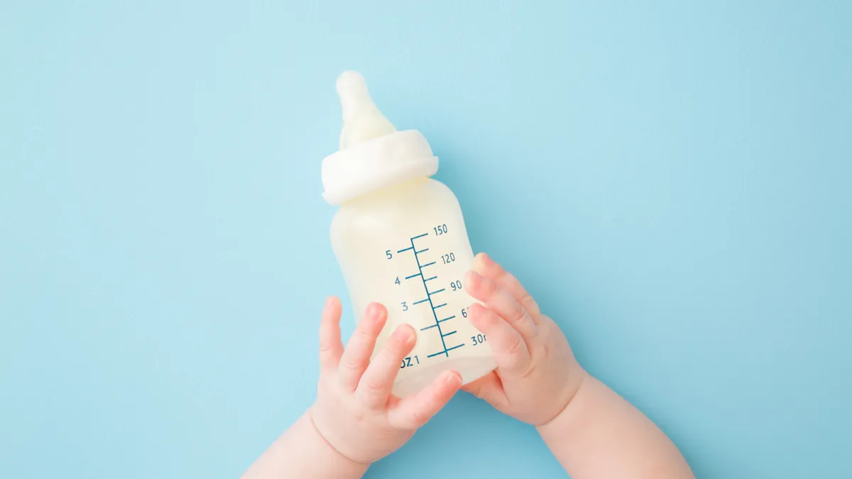 a baby's hands grab for a bottle of milk on a blue background