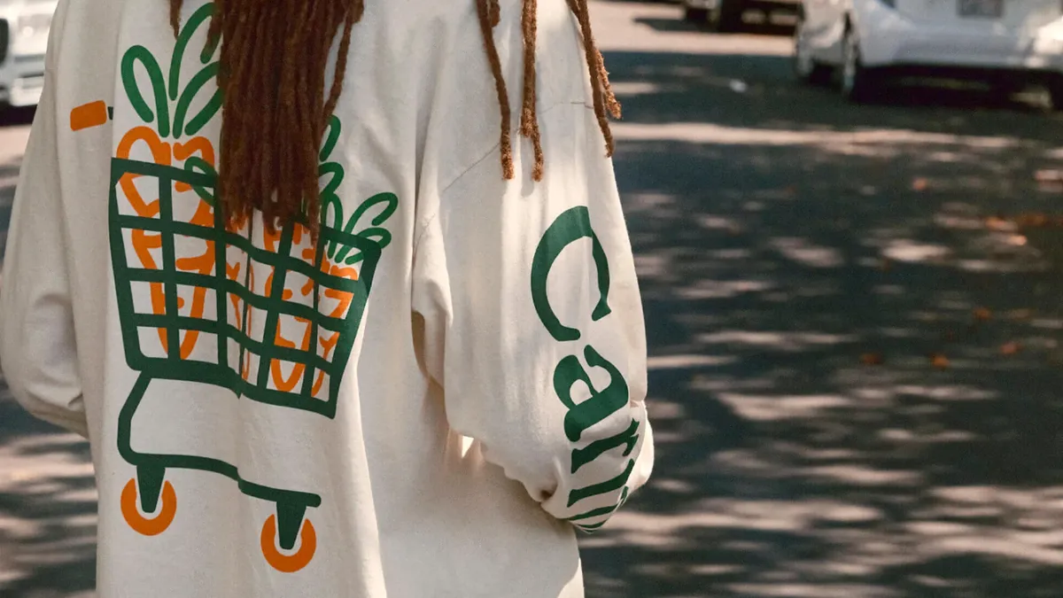 Close-up of the back of a shirt with a design illustration of four orange carrots in a green shopping cart.