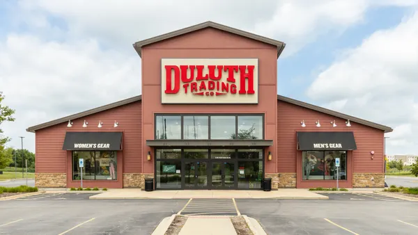 A brown building with two windows and a big door sitting in a parking lot. A sign says "Duluth Trading Co" in red letters.