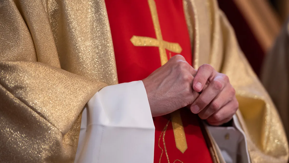 A person stands in gold religious robes with a cross on it.