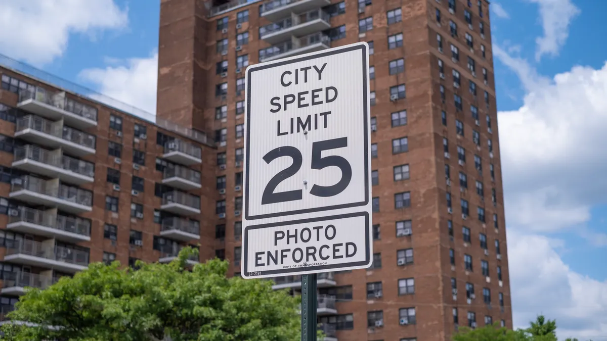 A 25 mph speed limit sign with a large apartment building in the background.