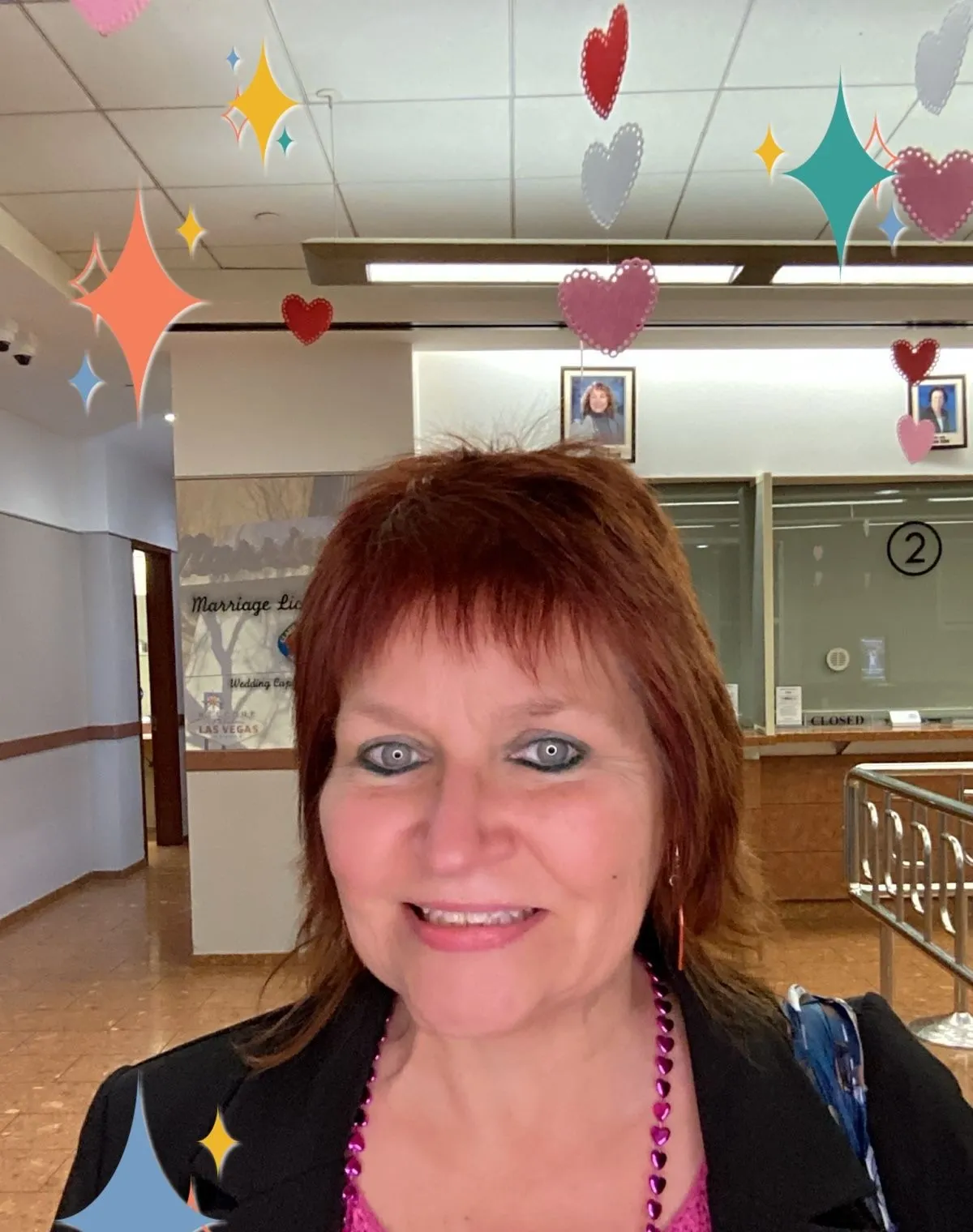 A person smiles at camera as paper hearts dangle from the ceiling above.