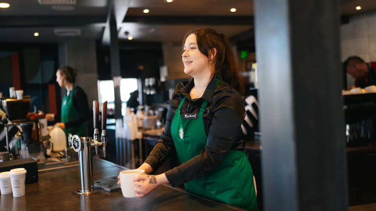 A Starbucks worker in a green apron and a black shirt.