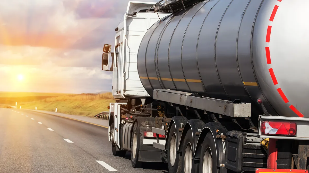 A tanker drives along the highway, toward the sun.