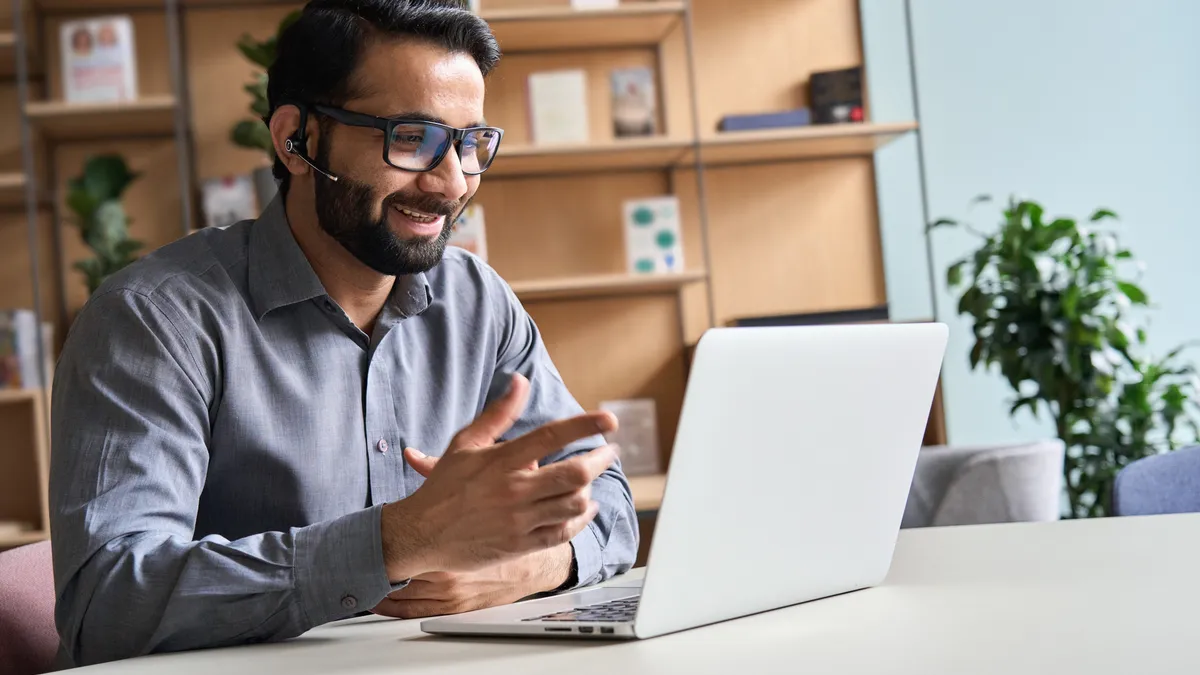 An Indian man wearing headset talking at virtual meeting