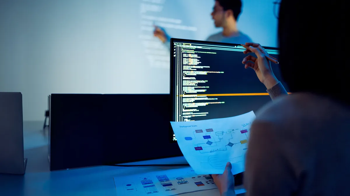 a tech training session featuring an instructor and a student sitting at their computer.