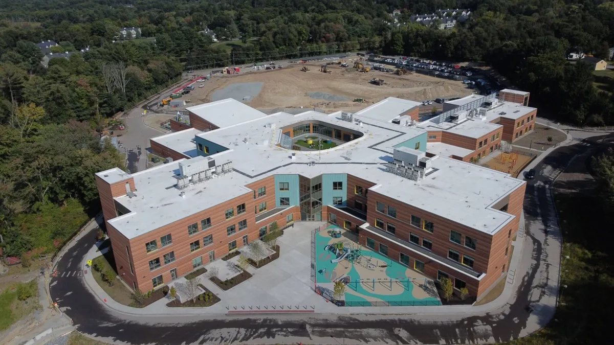 A sky shot of a school building, surrounded by woods, with a playground in the near part of the photo.