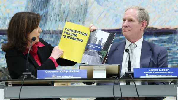 Woman holding a brochure that reads "Congestion pricing is working" while a man in a suit looks on.
