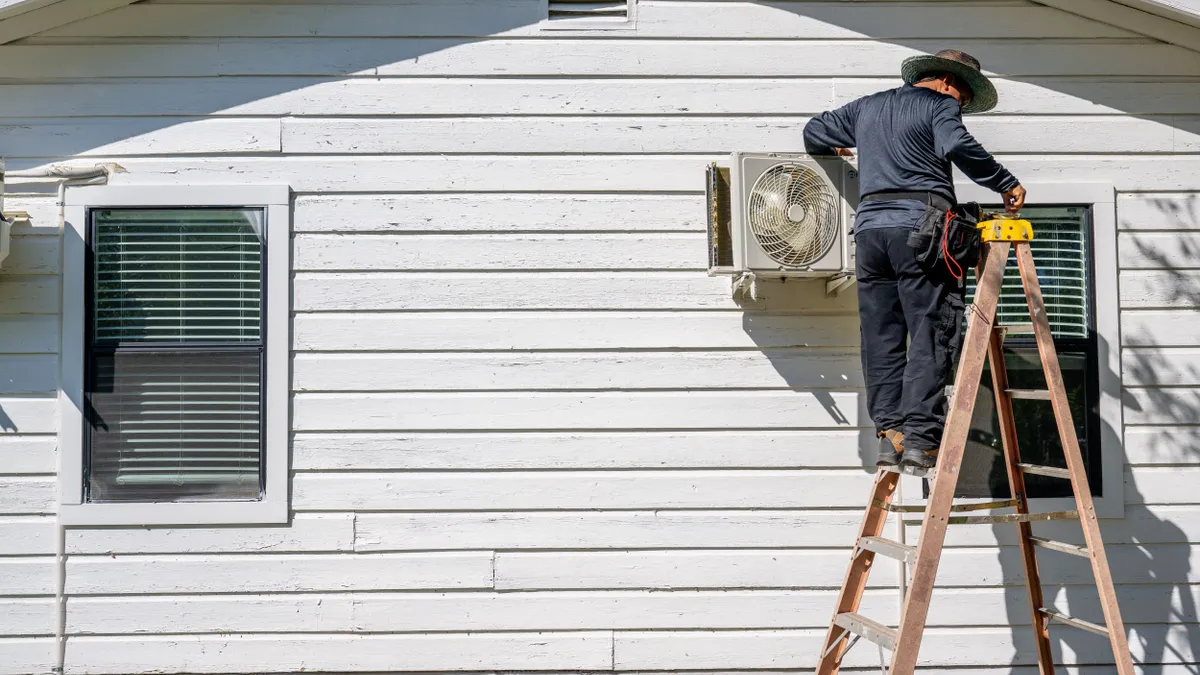 An individual stands on a ladder, working on an air conditioning unit.