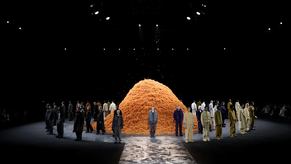 Models on a runway circle a giant fluffy orange pile.