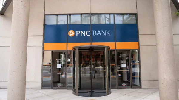 Exterior view of a PNC Bank branch with a revolving glass door. The building facade has large vertical columns. The PNC Bank sign features a blue and orange color scheme above the entrance.