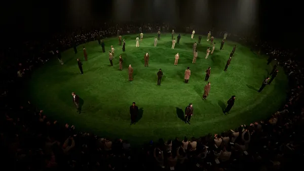 Men stand in a green indoor rotunda as part of a runway presentation.