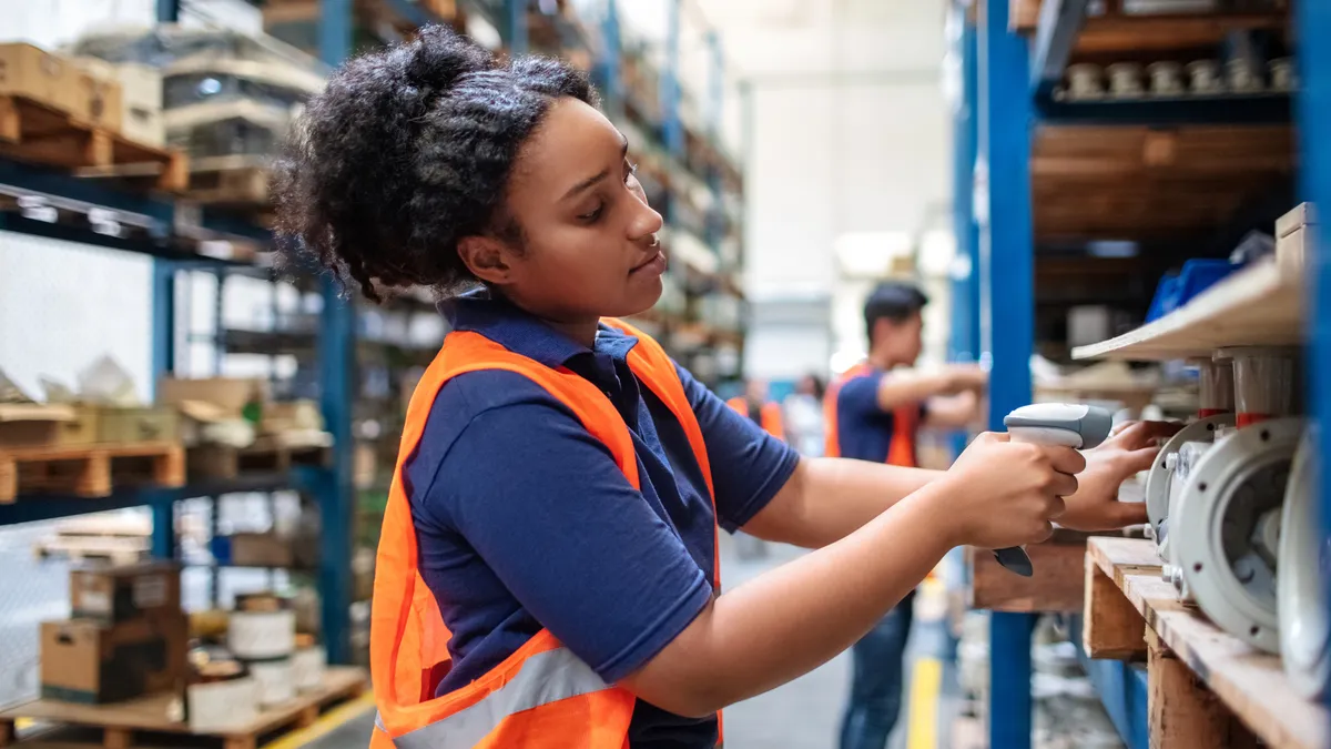 Warehouse worker checking cargo on shelves with scanner. Female worker in uniform scanning boxes in shelves.