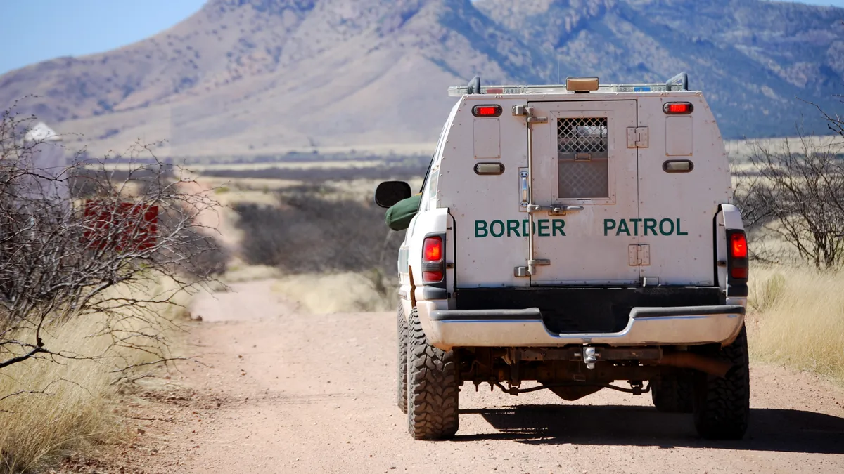 Back of a border patrol truck driving on a dirt road along the Mexican border in Arizona, with mountains in the background.