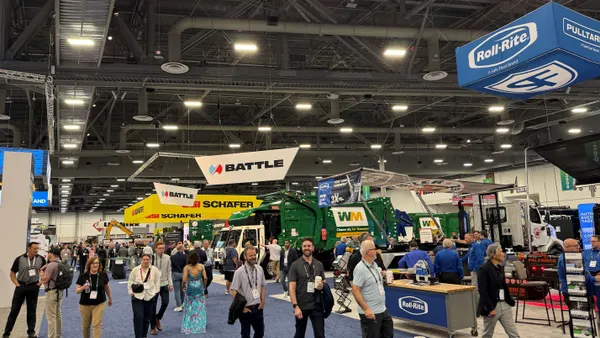 People walk by trash trucks in an exhibit hall.
