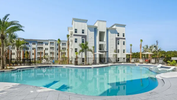 Light-colored new apartment property behind a swimming pool.