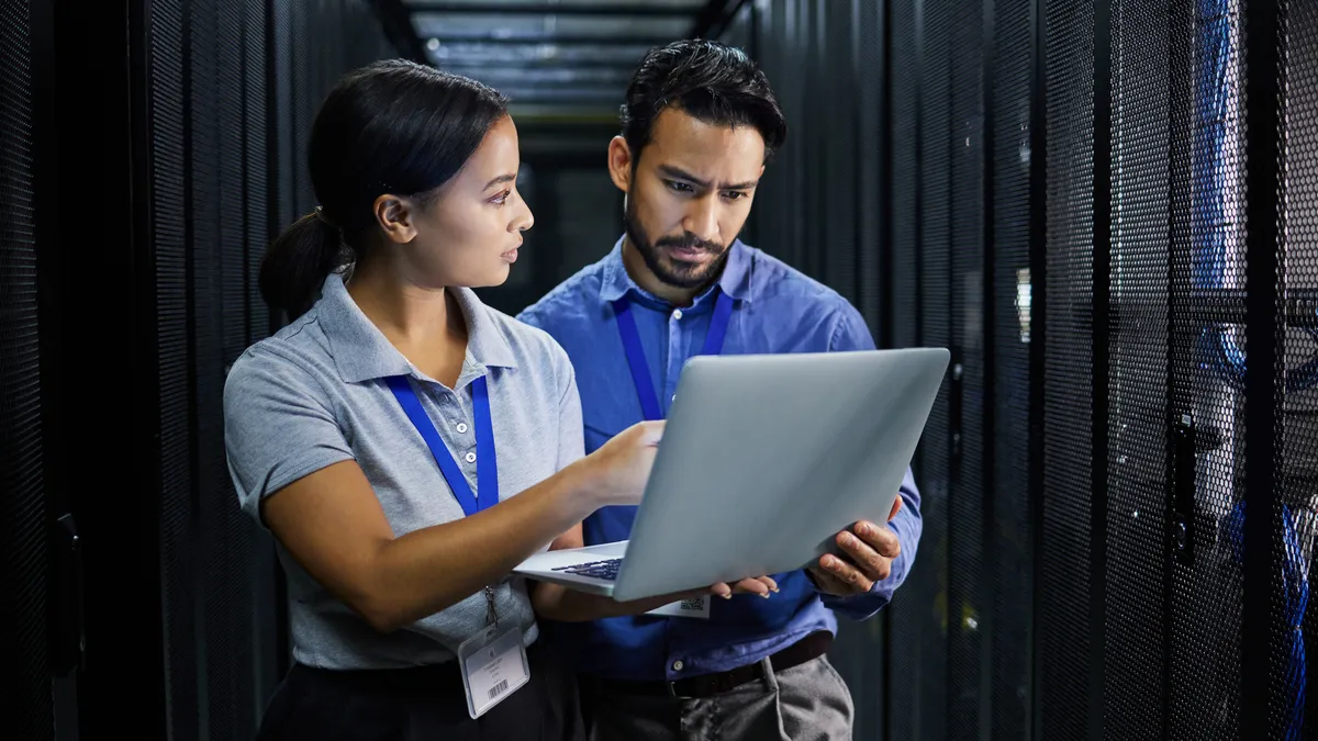 two technologists looking at a laptop inside a server room