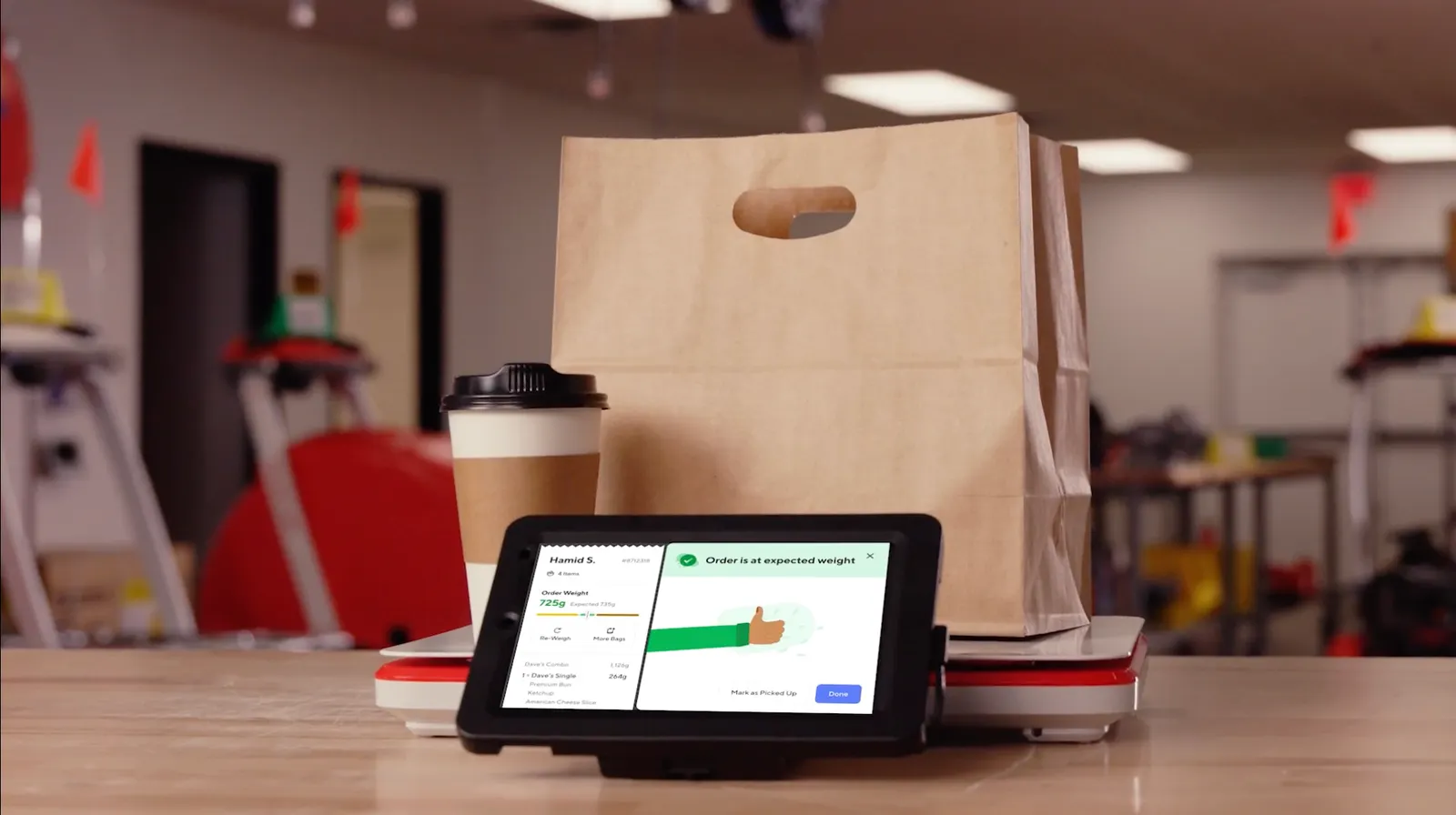 An image of a white scale with a bag and drink on it. A touchscreen says order is at expected weight.