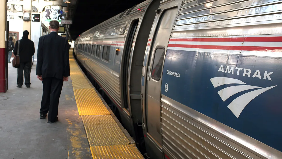 An Amtrak passenger train is stopped at Penn Station with passengers on the platform waiting to board.