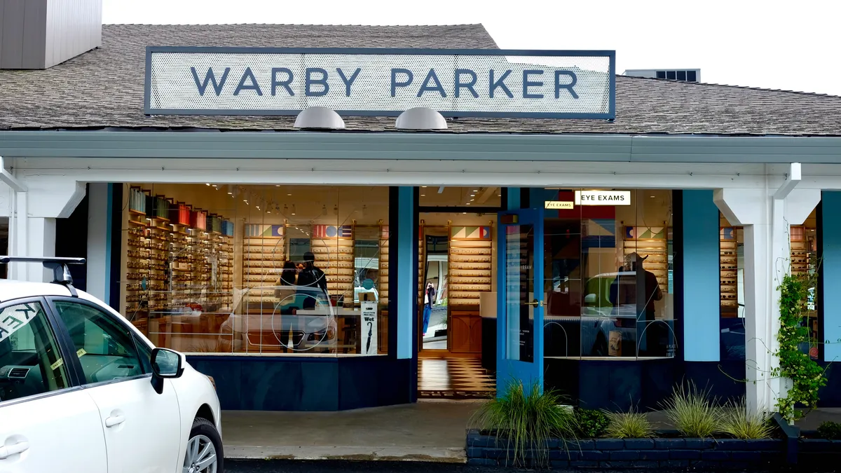 A white car is parked in front of a store, in a space toward the left.