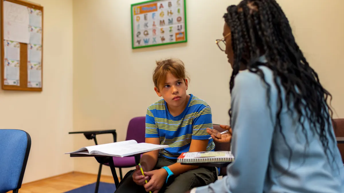 A student sits at a desk while listening to a school counselor.