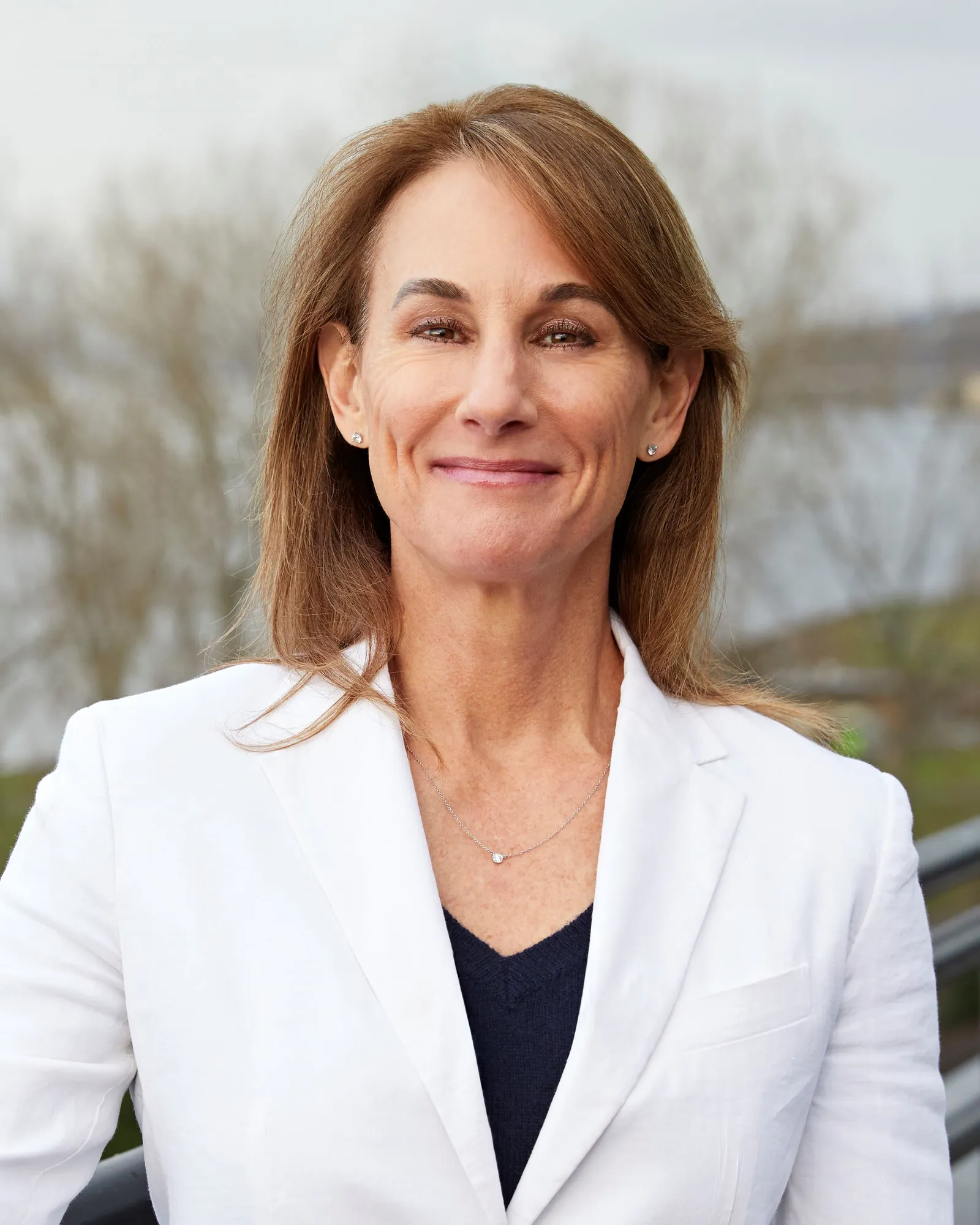 Headshot of a woman with light brown hair wearing a black shirt and a white blazer