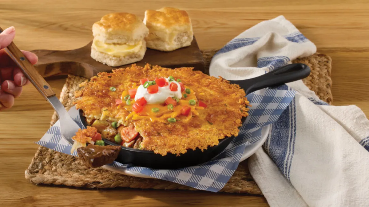 An image of a Hashbrown Shepherd's Pie offered in a cast iron skillet. A hand with a fork has beef at the end.