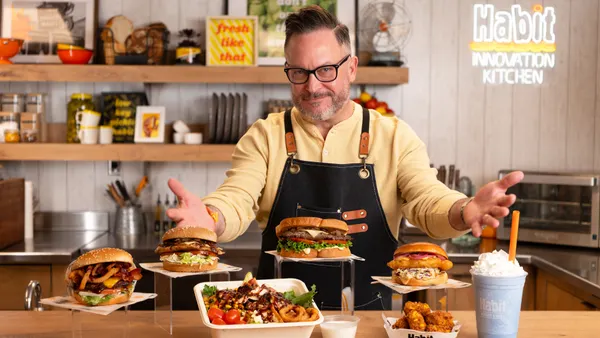 A person holds their arms out to showcase various sandwiches, salads and burgers from Habit Burger