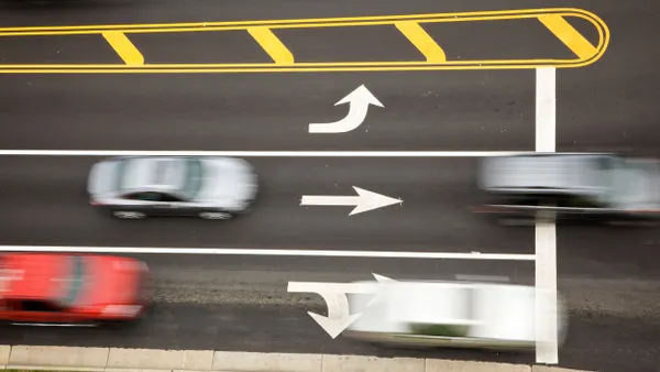 Aerial view of four cars driving in three lanes with white directional arrows.