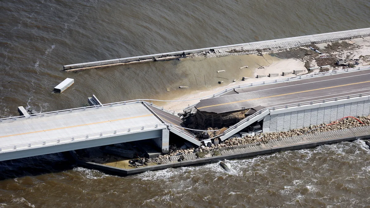 Aerial view shows a road stretching through water with heavy damage in the middle.