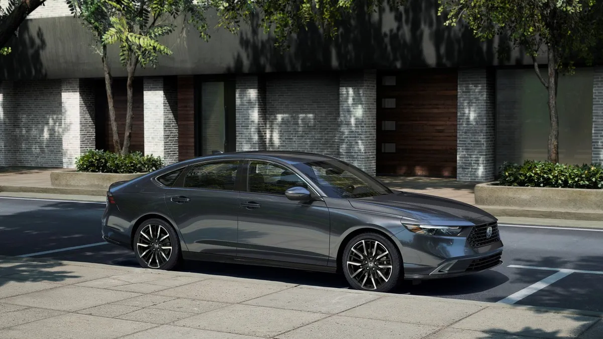 A gray 2024 Honda Accord Touring parked in front of a building with tress in the background.