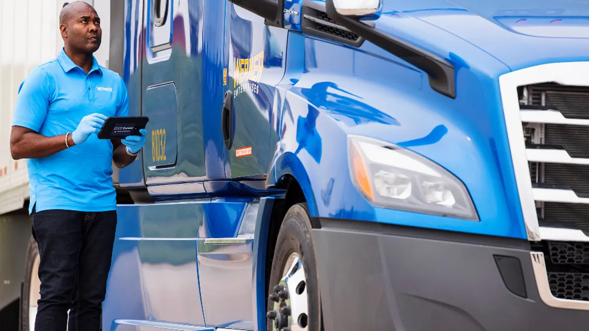 A Werner employee works on a Werner Edge tablet next to a truck.