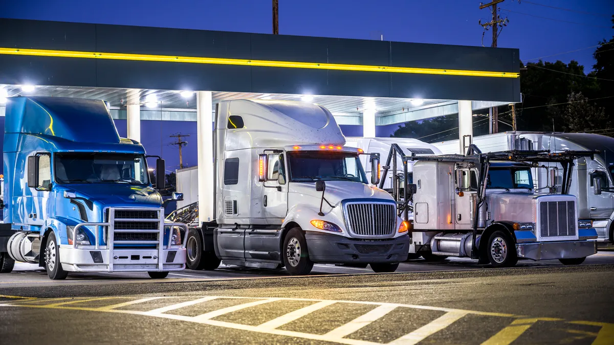 Trucks at a rest stop at night with lights shining.