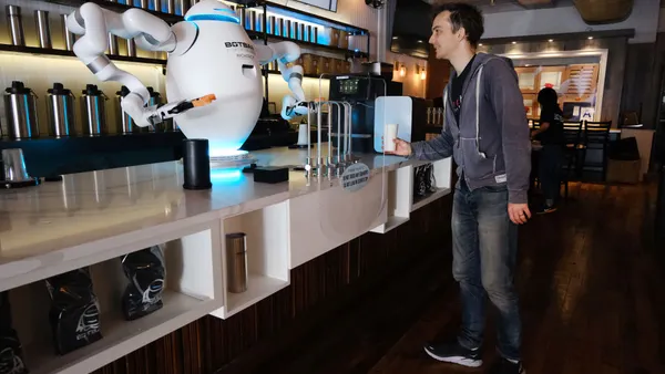 A smiling man approaches a white counter where a white robot is preparing an espresso drink.