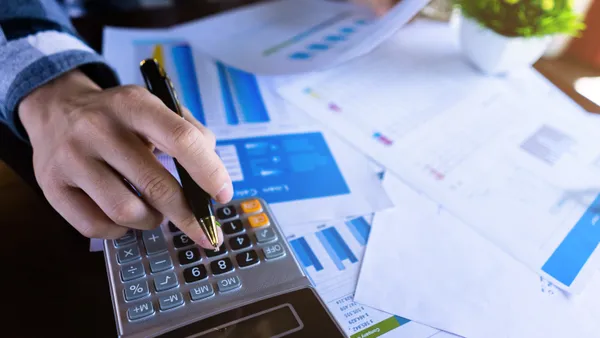 Close up of a person using a calculator and reading paper document about business data.