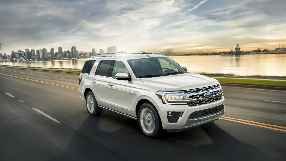 A white 2023 Ford Expedition SUV driving on a road with a city skyline in the background.